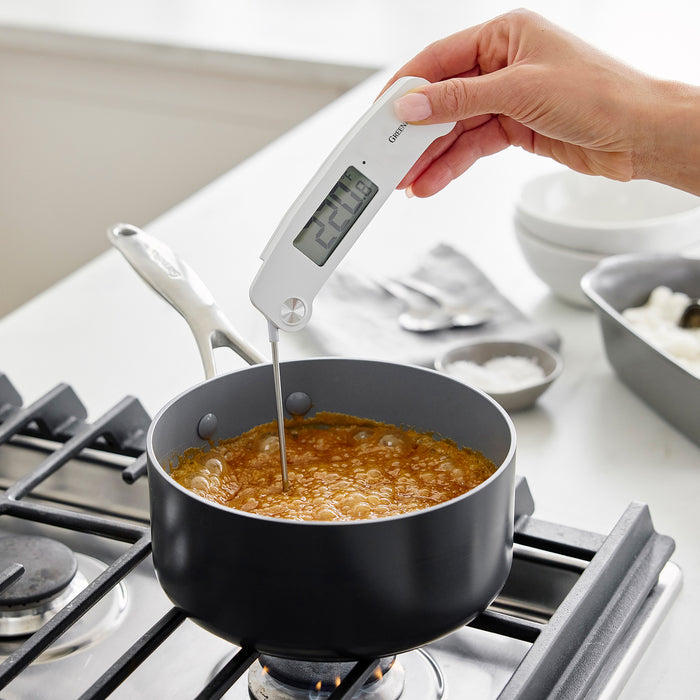 Hand holding digital kitchen thermometer in bubbling pot on stove, display reads 224.8°F.