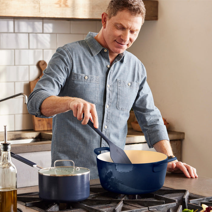 Cobalt blue enameled cast iron Dutch oven by GreenPan on stove, being stirred with a utensil.
