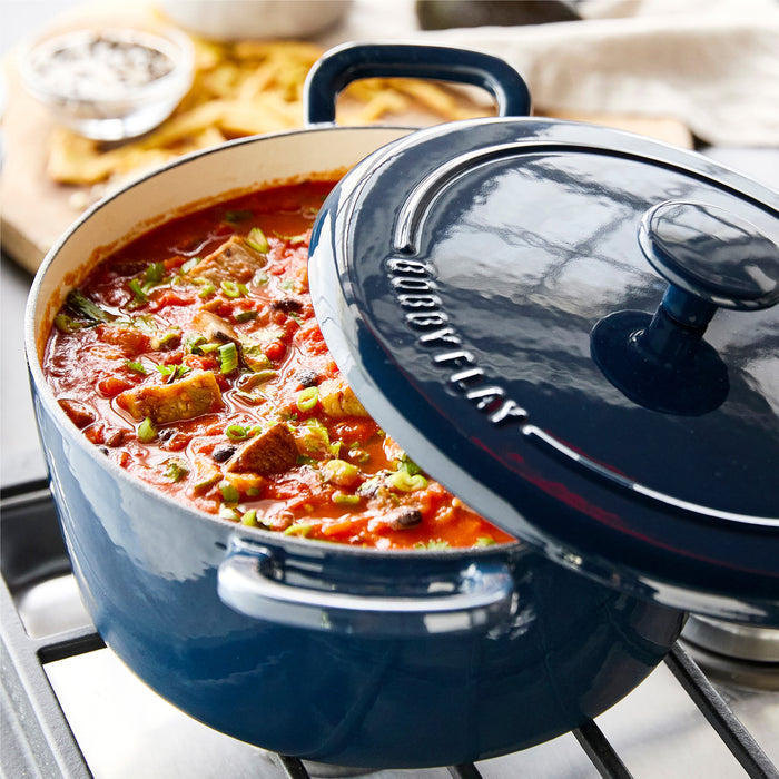 Cobalt blue Dutch oven on stove filled with tomato stew, garnished with green onions.