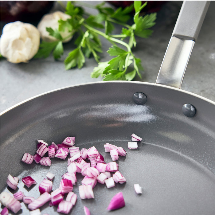 Diced red onions in a stainless steel frypan with lid, 12-inch size, on a kitchen surface.