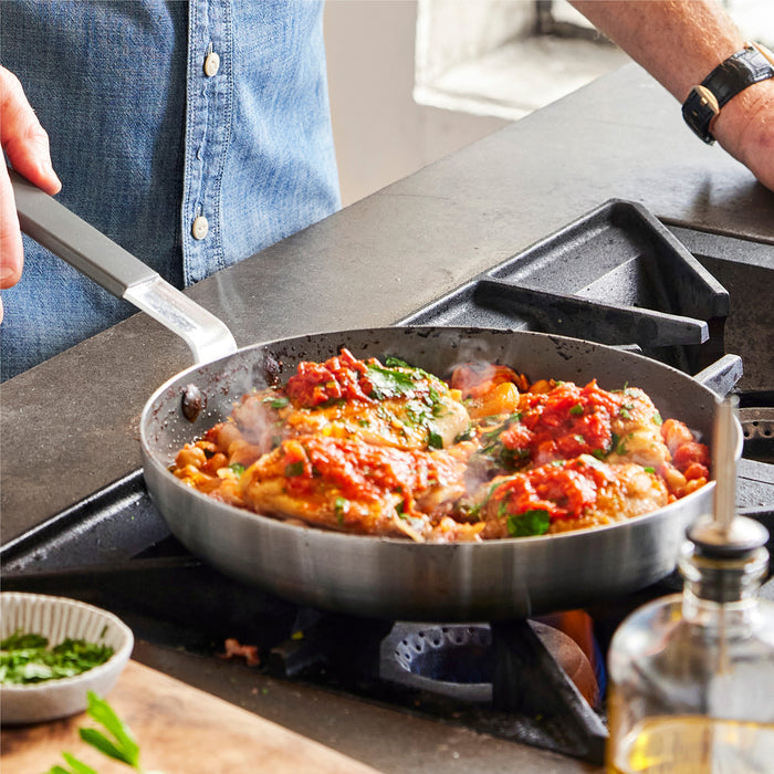 Chicken with tomato sauce and greens cooking in a GreenPan 12-inch nonstick frypan, lid placed to the side.