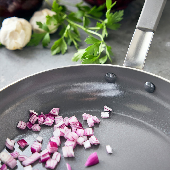 Diced red onion in a stainless steel frypan with parsley and garlic visible in the background.
