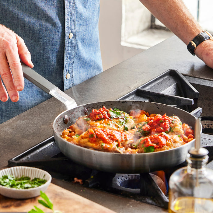 Person in blue shirt uses Bobby Flay by GreenPan stainless steel frypans to cook tomato chicken on the stove.