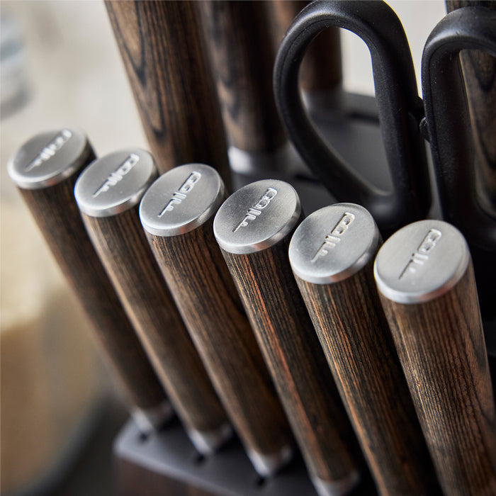 Close-up of the Bobby Flay by GreenPan Stainless Steel 13-Piece Knife Block Set, featuring wooden handles, stainless steel blades, metal ends, and kitchen scissors, all neatly arranged in a stylish knife block.