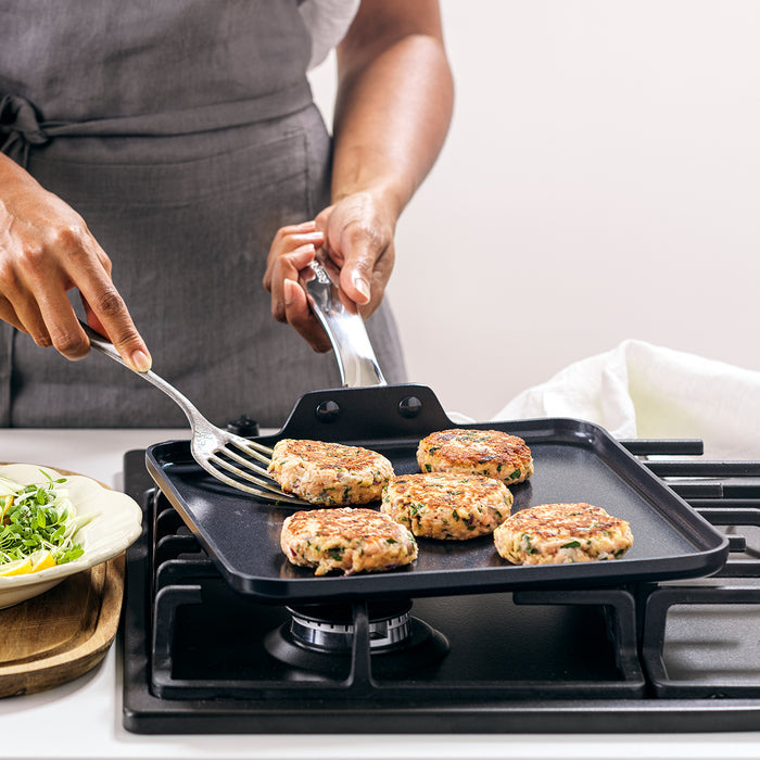 Flipping patties on a black ceramic square griddle with fresh greens beside the pan.
