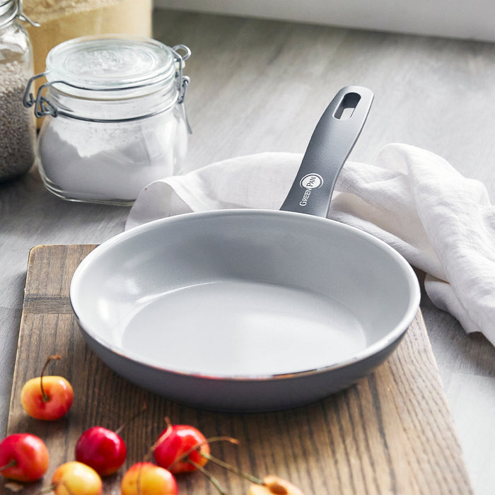 Ceramic nonstick 8-inch frypan with a stay-cool handle on a wooden board, cherries and jars in the background.