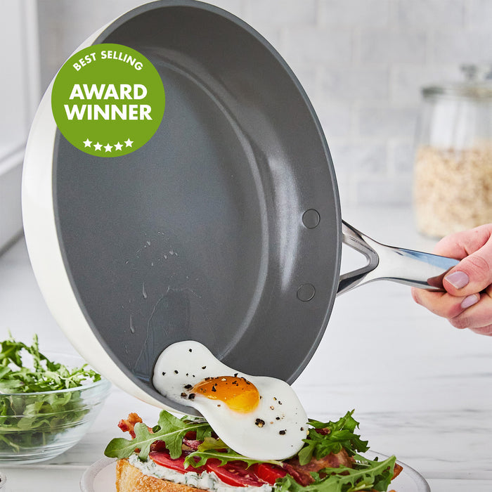 Fried egg slides from colorful ceramic frypan onto toast with greens; pan features an Award Winner label.