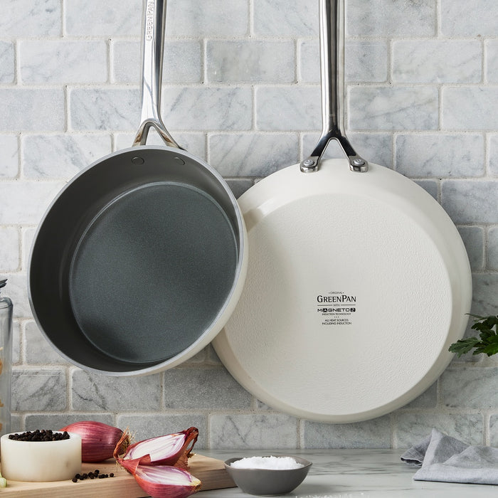 Set of two cream-colored ceramic frypans with shiny handles, displayed on a marble surface.