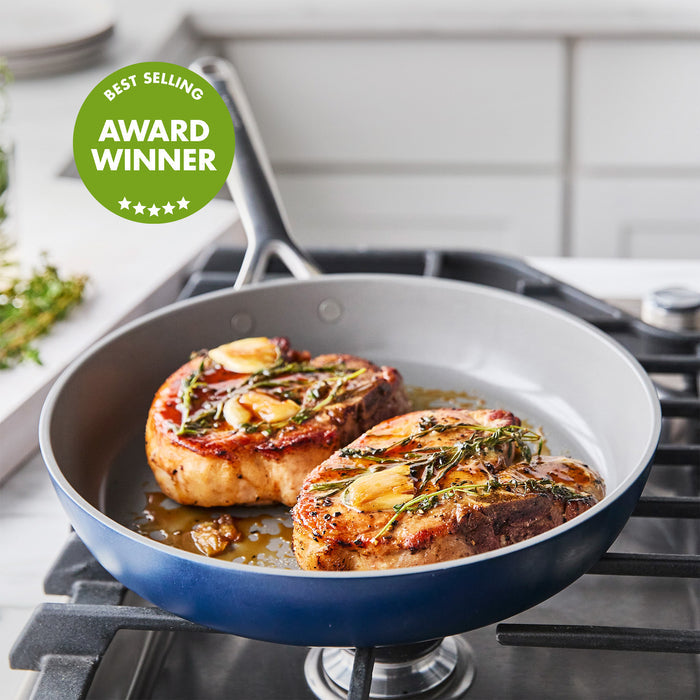 Two pork chops with herbs and garlic cooking in a colorful ceramic nonstick frypan set, Best Selling Award Winner badge visible.
