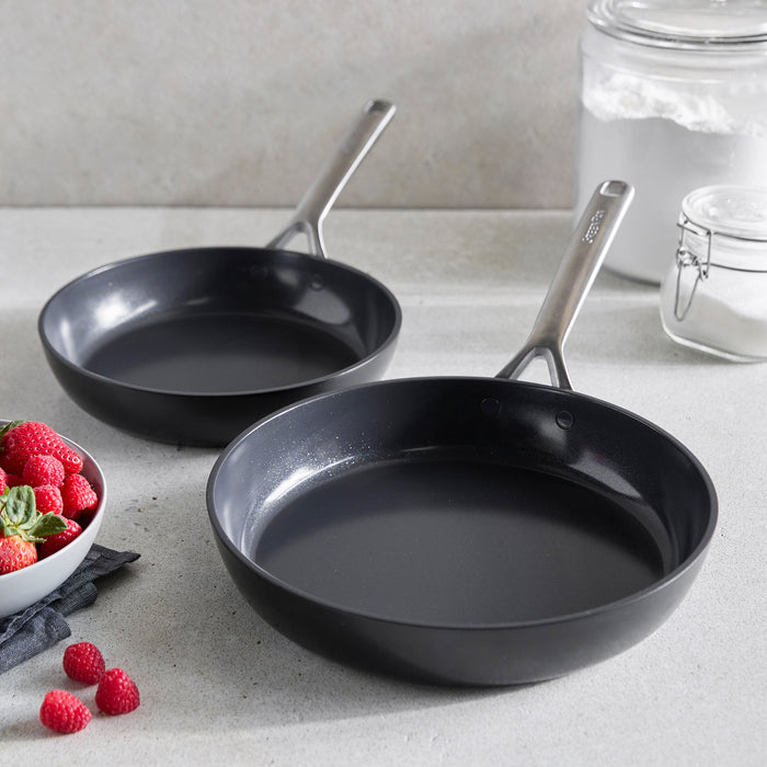 Two ceramic nonstick frypans, 9.5 and 11, on a counter near strawberries and glass jars.