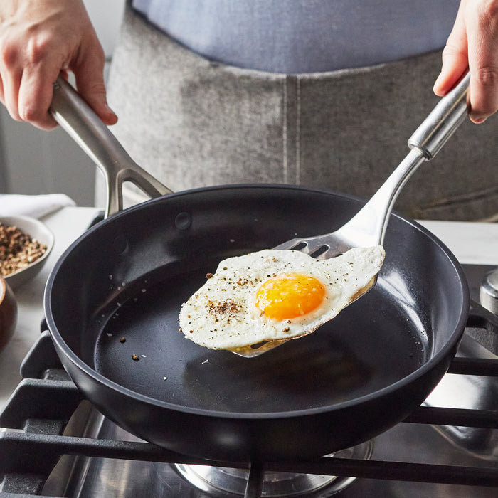 Sunny-side-up egg lifted from a set of two GP5 Infinite8 ceramic nonstick frypans with a spatula.