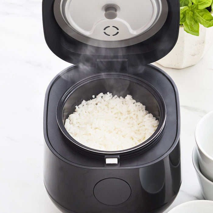 Black 4-cup rice cooker with open lid, showing steamed rice inside a ceramic pot.