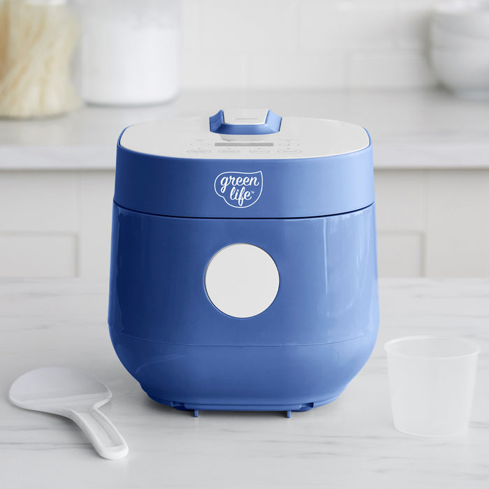 Blue 4-cup rice and grains cooker on a kitchen counter with matching rice paddle and measuring cup.