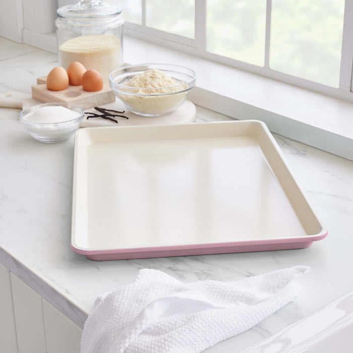 Pink ceramic cookie sheet on a countertop with baking ingredients nearby.