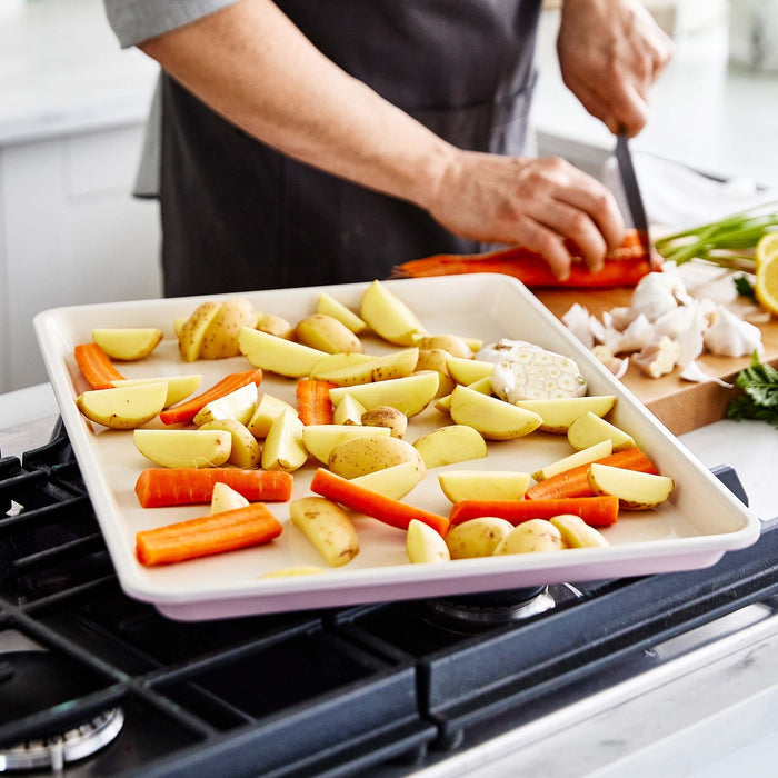 Chopping carrots beside a pink GreenLife ceramic nonstick cookie sheet with sliced vegetables.
