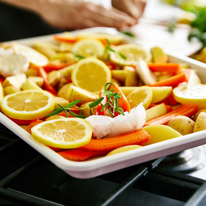 Carrots, potatoes, lemons, garlic, and rosemary arranged on a pink GreenLife baking sheet ready for roasting.
