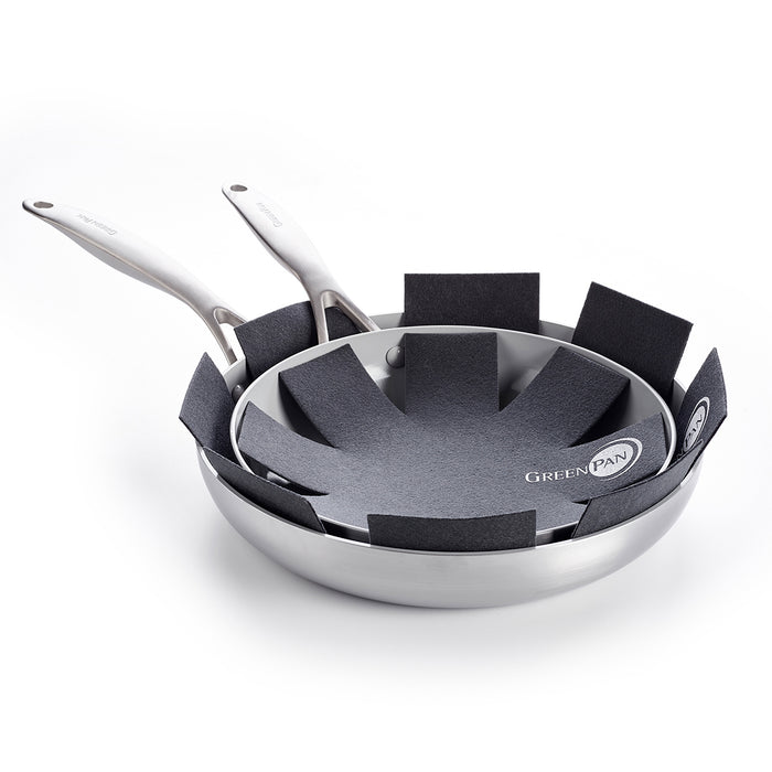 Two metal nonstick pans with silver handles are stacked, separated by a GreenPan 3 Pan Protector to prevent scratches. The bottom pan displays the GreenPan logo.