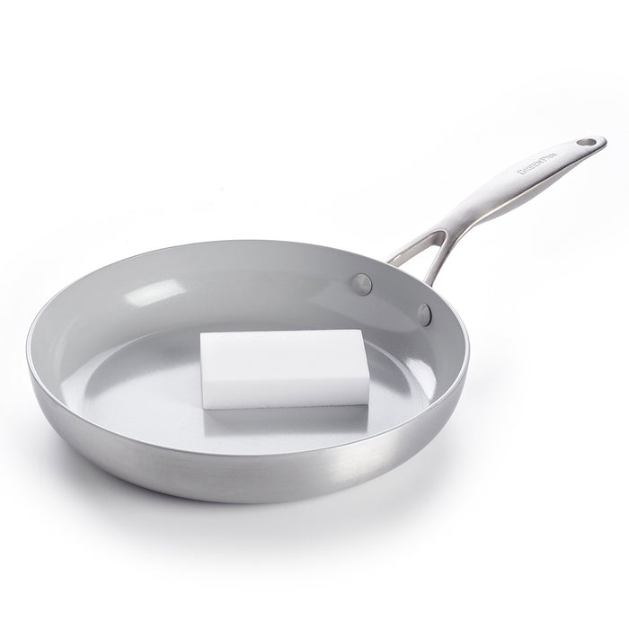 Two white melamine sponges in a pack rest inside a clean stainless steel frying pan with a handle.