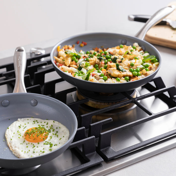 Ceramic nonstick frypan set on a stove, one pan with a fried egg, another with stir-fried chicken and vegetables.