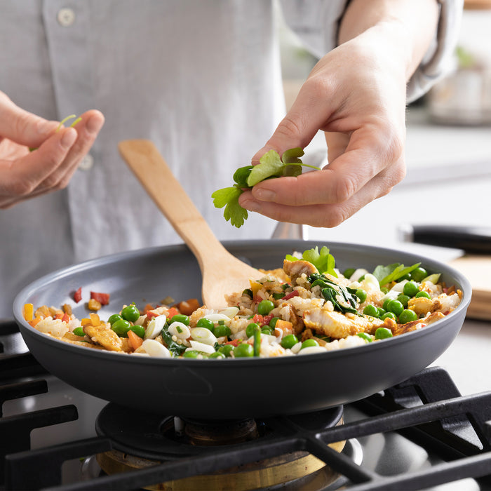 Stir-fried rice and veggies with herbs in a green ceramic nonstick frypan, stirred with a wooden spoon.