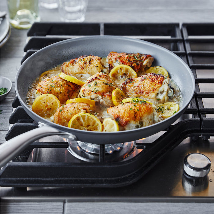 Chicken and lemon in sauce cooking in a green ceramic nonstick frypan set on a gas stove.