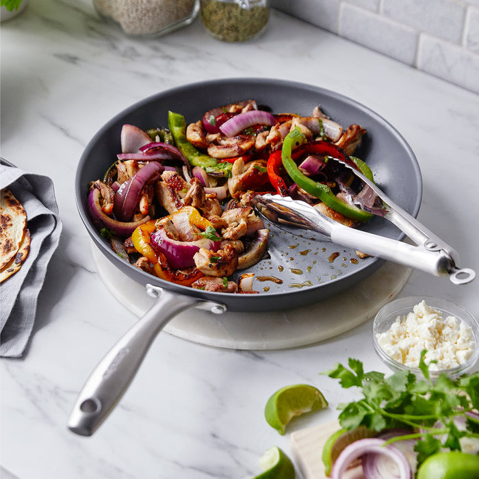 Set of three ceramic nonstick frypans 8, 10, 12 with sautéed chicken, peppers, and onions on a marble countertop.