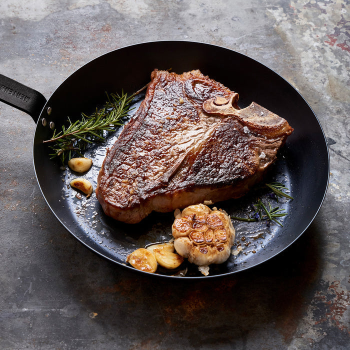 T-bone steak with garlic and rosemary in a black Merten  Storck carbon steel 10-inch frypan.