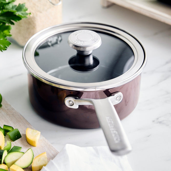 Chocolate brown 2-quart saucepan with matching lid, shown on a kitchen surface near fresh vegetables.