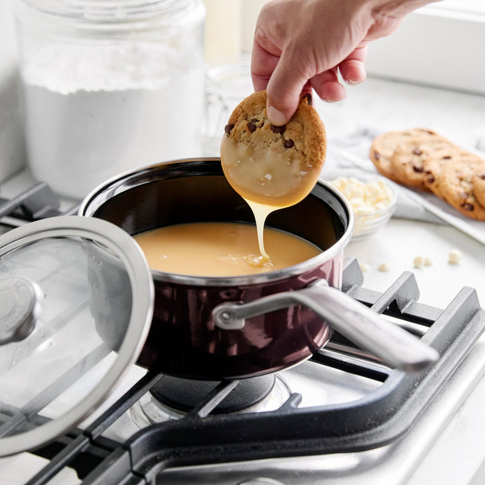 Hand dipping a cookie into melted white chocolate in a blue Merten  Storck enameled steel 2-quart saucepan.