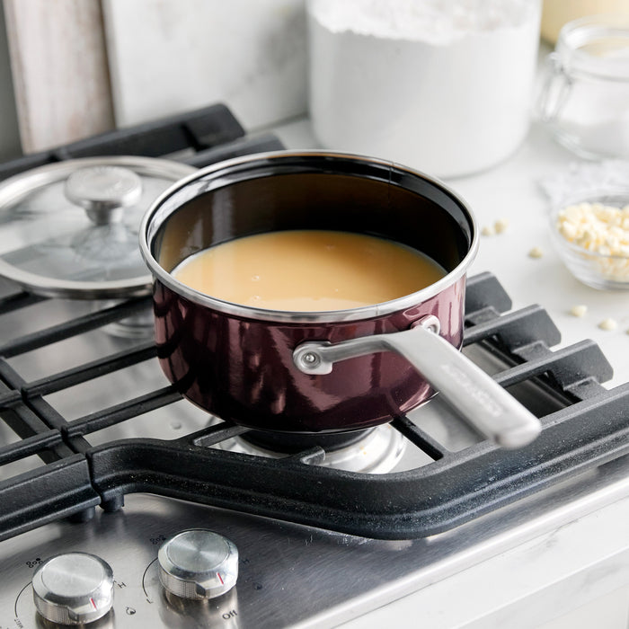 Chocolate brown enameled steel 2-quart saucepan with lid shown on a stove, sauce visible inside.