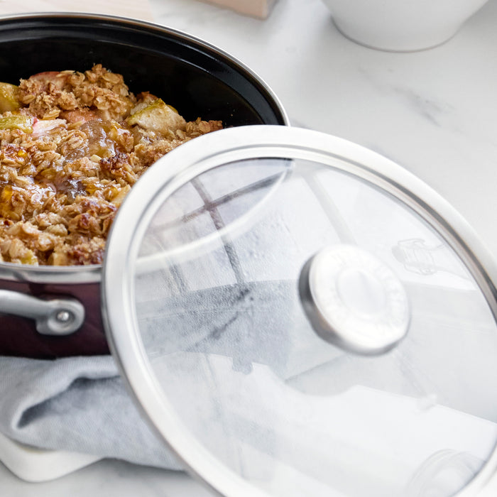 Chocolate brown 2-quart sauté pan with lid, holding crumble dessert, on a gray cloth countertop.