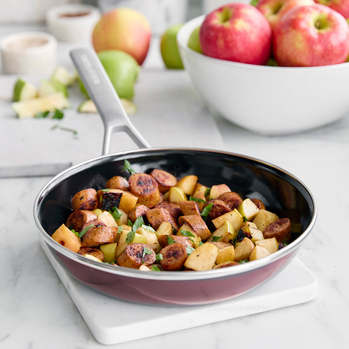 Cooked sausage and diced apples in a Merten  Storck 9.5 frypan on white surface, bowl of apples in background.