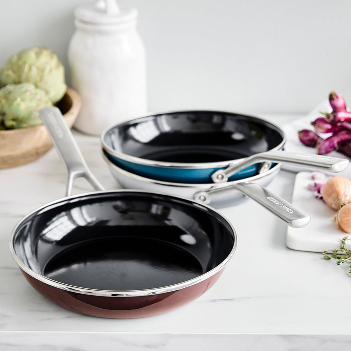 Chocolate brown enameled steel frypan on a marble countertop with assorted vegetables nearby.