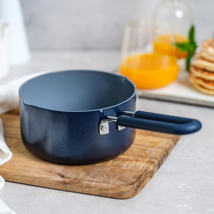 Navy ceramic nonstick 1-quart saucepan on a wooden board, with juice and pancakes in the background.