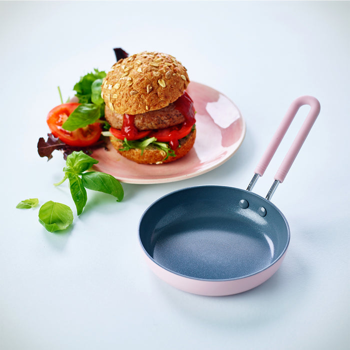 Pink ceramic nonstick mini frypan next to a veggie burger with lettuce, tomato, and fresh herbs.