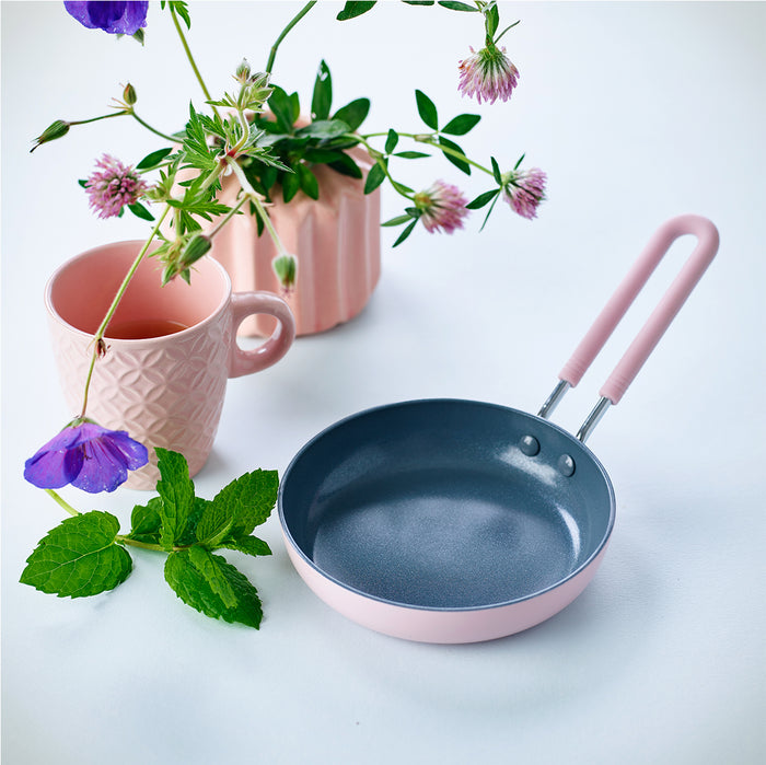 Pink ceramic cup, pink mini 5-inch ceramic frypan, and flower vase with mint leaves on a white surface.