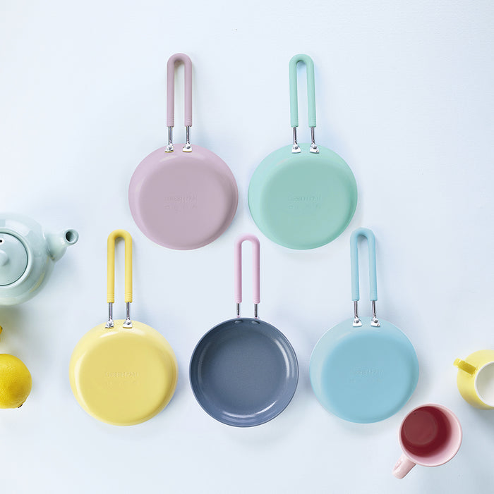 Set of five yellow ceramic mini frypans with matching handles, displayed on a light surface with lemons and kitchen items.