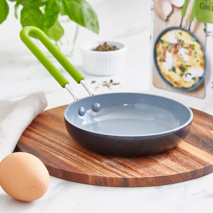 Green ceramic nonstick mini frypan resting on a wooden board with an egg and recipe card nearby.