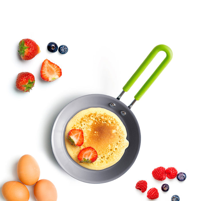 Green mini ceramic nonstick round frypan with pancake, strawberries, eggs, mixed berries, and green spatula.