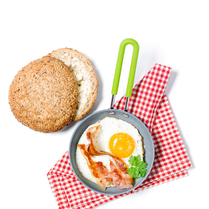 Mini ceramic nonstick round frypan with fried egg, bacon, parsley, and a sesame bun on a red checkered napkin.