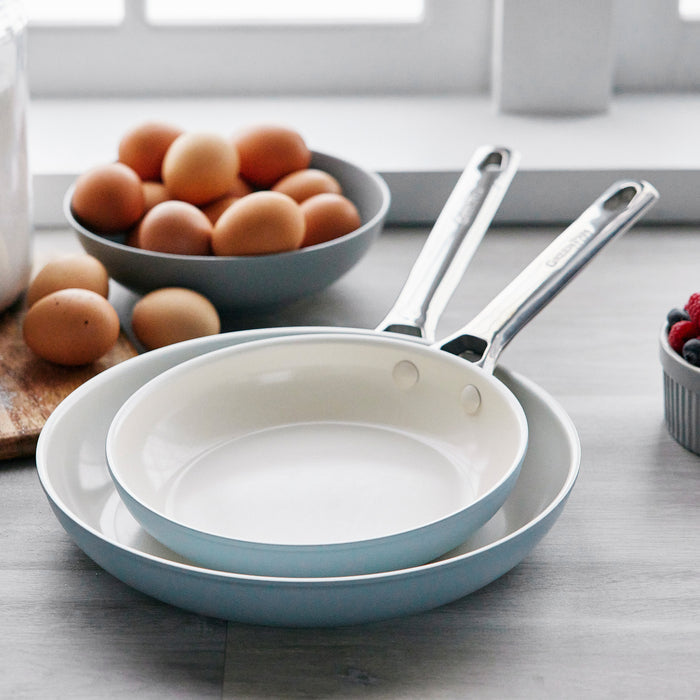 Two ceramic nonstick frypans, 8 and 10, stacked on a counter with eggs and berries nearby.