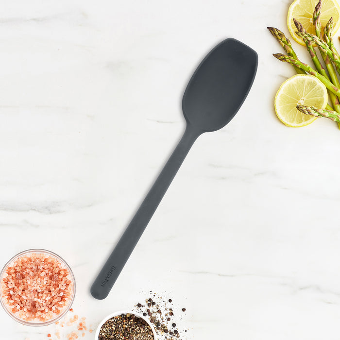 Gray platinum silicone flat head spoon rests on marble next to asparagus spears and lemon slices.