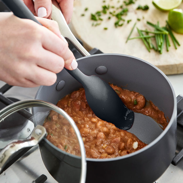 Gray platinum silicone flat head spoon stirring refried beans on a stove, with herbs and lime nearby.