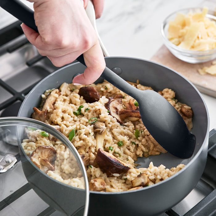 Gray platinum silicone flat head spoon stirs mushroom risotto in a pan, with a bowl of grated cheese nearby.