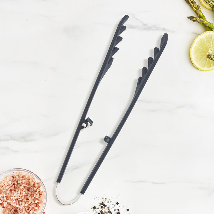 Gray silicone pasta tongs with scalloped edges next to salt, pepper, lime wedges, and asparagus spears.