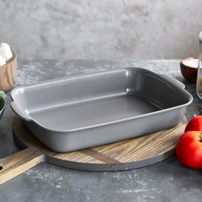 Gray ceramic rectangular baker on a cutting board with assorted fresh vegetables nearby.