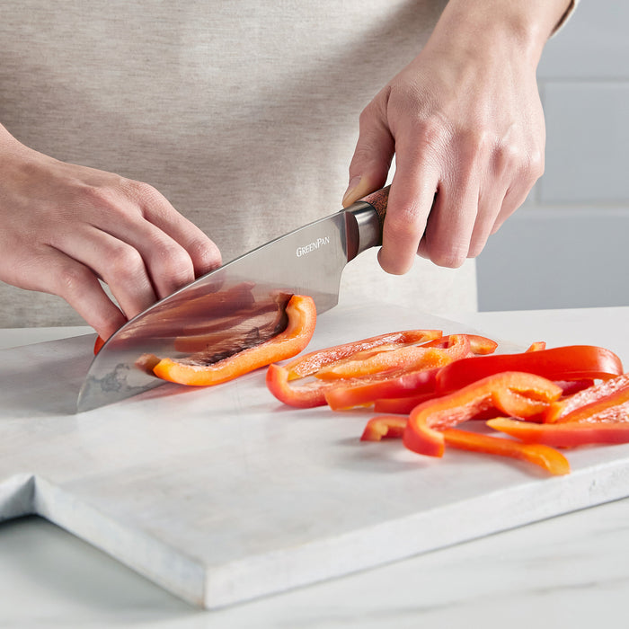 Slicing red bell peppers on a white board with a stainless steel Santoku knife featuring a walnut handle.