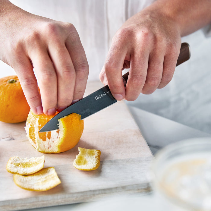 Hands peeling an orange with a 4-inch paring knife featuring a walnut handle on a cutting board.