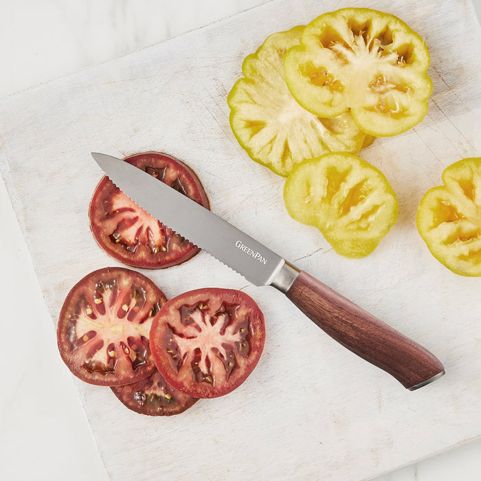 Serrated utility knife with walnut handle slicing green and purple tomatoes on a white cutting board.