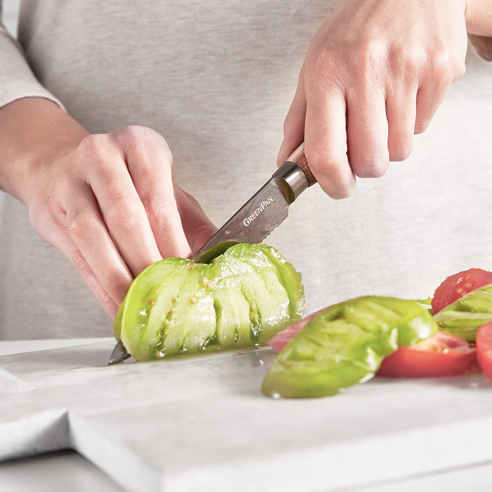 Slicing a green tomato with a 5-inch serrated utility knife with a walnut handle on a white board.